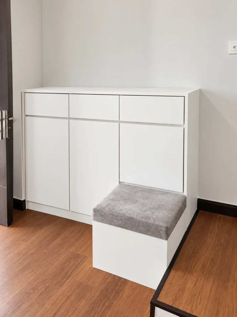 White Entry Shoe Cabinet With Three Top Drawers And A Grey Upholstered Seat.