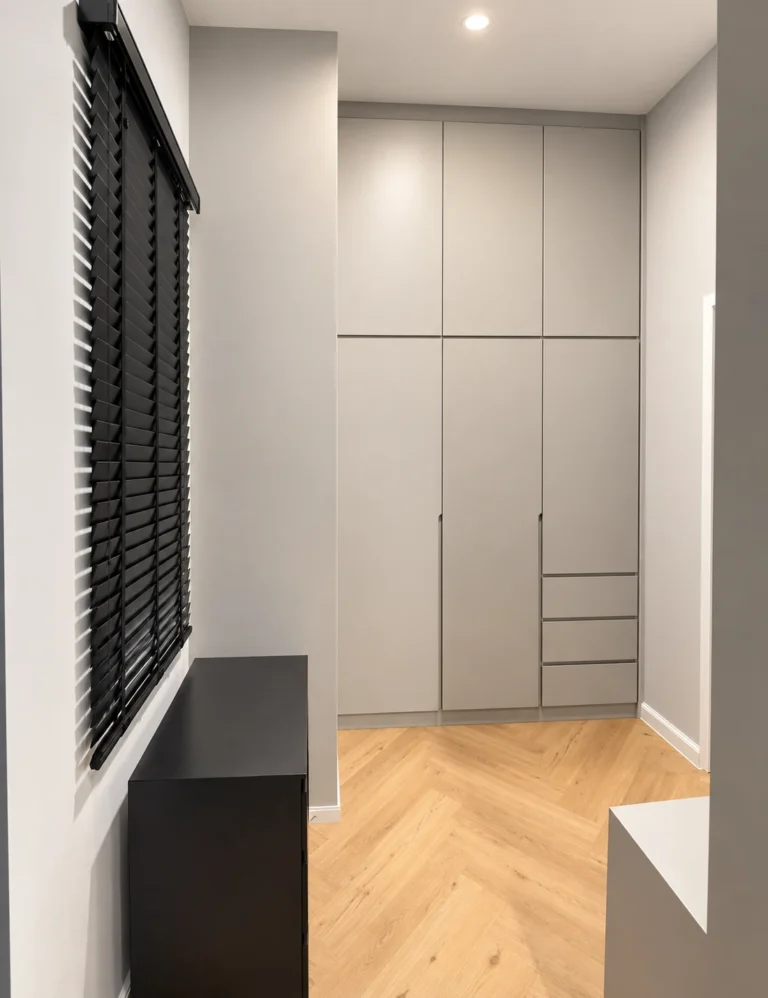 Pale Handleless Wardrobe And Drawers Beside Black Blinds And A Herringbone Floor.